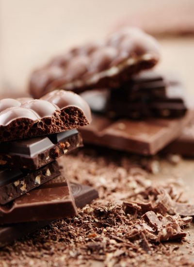 Composition of bars and pieces of different milk and dark chocolate, grated cocoa on a brown background side view close up