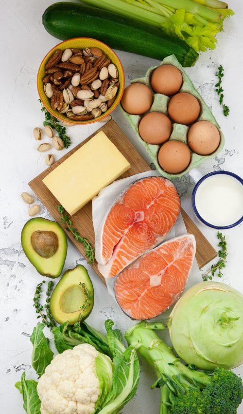 Ketogenic low carbs diet concept. A set of products of the healthy balanced food. Green vegetables, avocado, nuts, salmon, eggs, milk products. Healthy food concept. White background, top view, copy-space